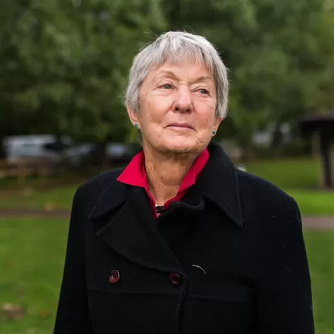 Permaculture Teacher and Author Rosemary Morrow, standing outside, wearing a black sweater over a red shirt.