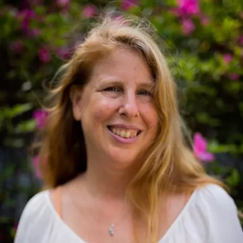 Laura Oldanie wearing a white shirt in front of flowers bushes with red blossoms. Text on the image reads Permaculture Values and Impact Investing Laura Oldanie