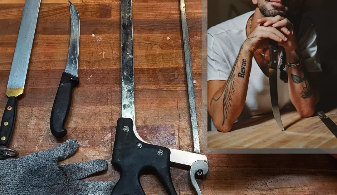 Background: a butcher block table with the tools of this craft on top, including two knives, a bone saw, and a cut-resistant glove. In the upper right hand corner, is an inset picture of Andrew Magazine with his chin resting on this hands and a broad brimmed hat on his head against a dark background.