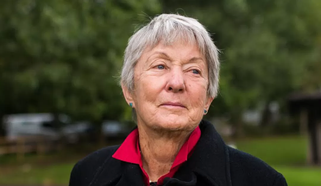 Permaculture Teacher and Author Rosemary Morrow, standing outside, wearing a black sweater over a red shirt.